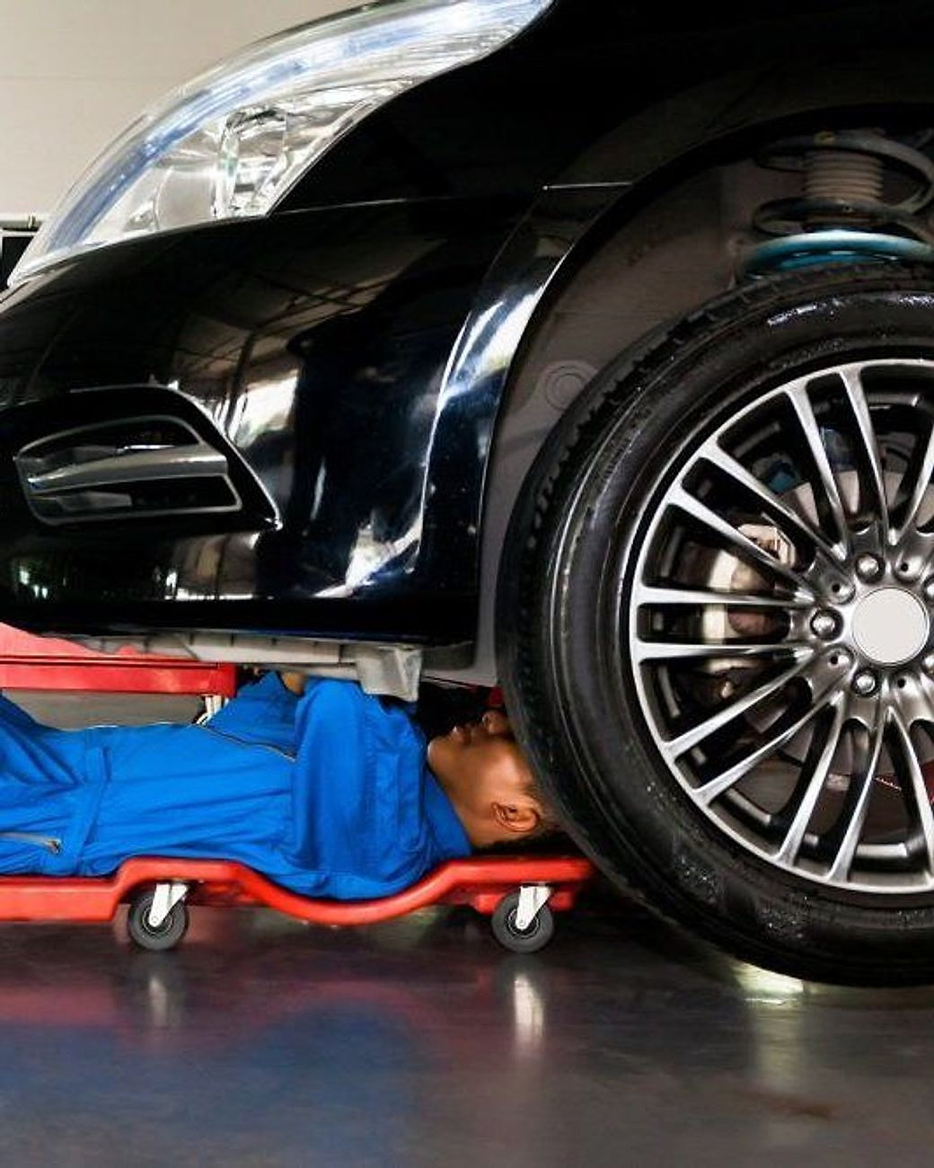 Un meccanico disteso sul carrello lavora sotto un auto sollevata in officina.